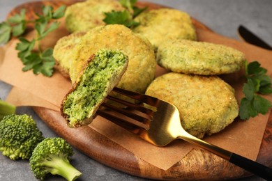 Photo of Fork with piece of delicious broccoli cutlet and parsley on wooden board, closeup. Vegan dish