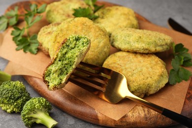 Fork with piece of delicious broccoli cutlet and parsley on wooden board, closeup. Vegan dish