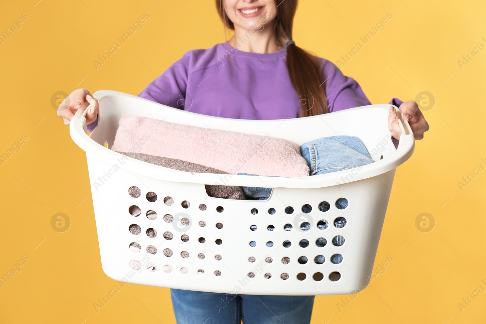 Photo of Young woman holding laundry basket with clothes on color background, closeup