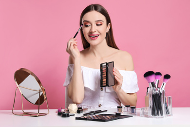 Beauty blogger applying eyeshadow on pink background