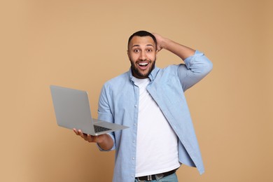 Photo of Surprised young man with laptop on beige background