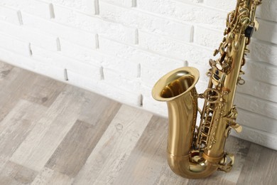 Photo of Beautiful saxophone on floor near white brick wall indoors, closeup. Space for text