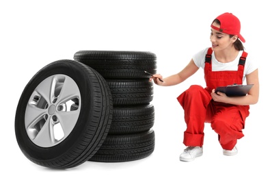 Female mechanic in uniform with car tires and clipboard on white background