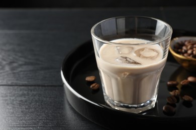 Photo of Coffee cream liqueur in glass and beans on black wooden table, closeup. Space for text