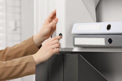 Photo of Woman taking folder with documents from shelf in office, closeup