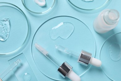 Petri dishes with samples of cosmetic serums, bottle and pipettes on light blue background, flat lay