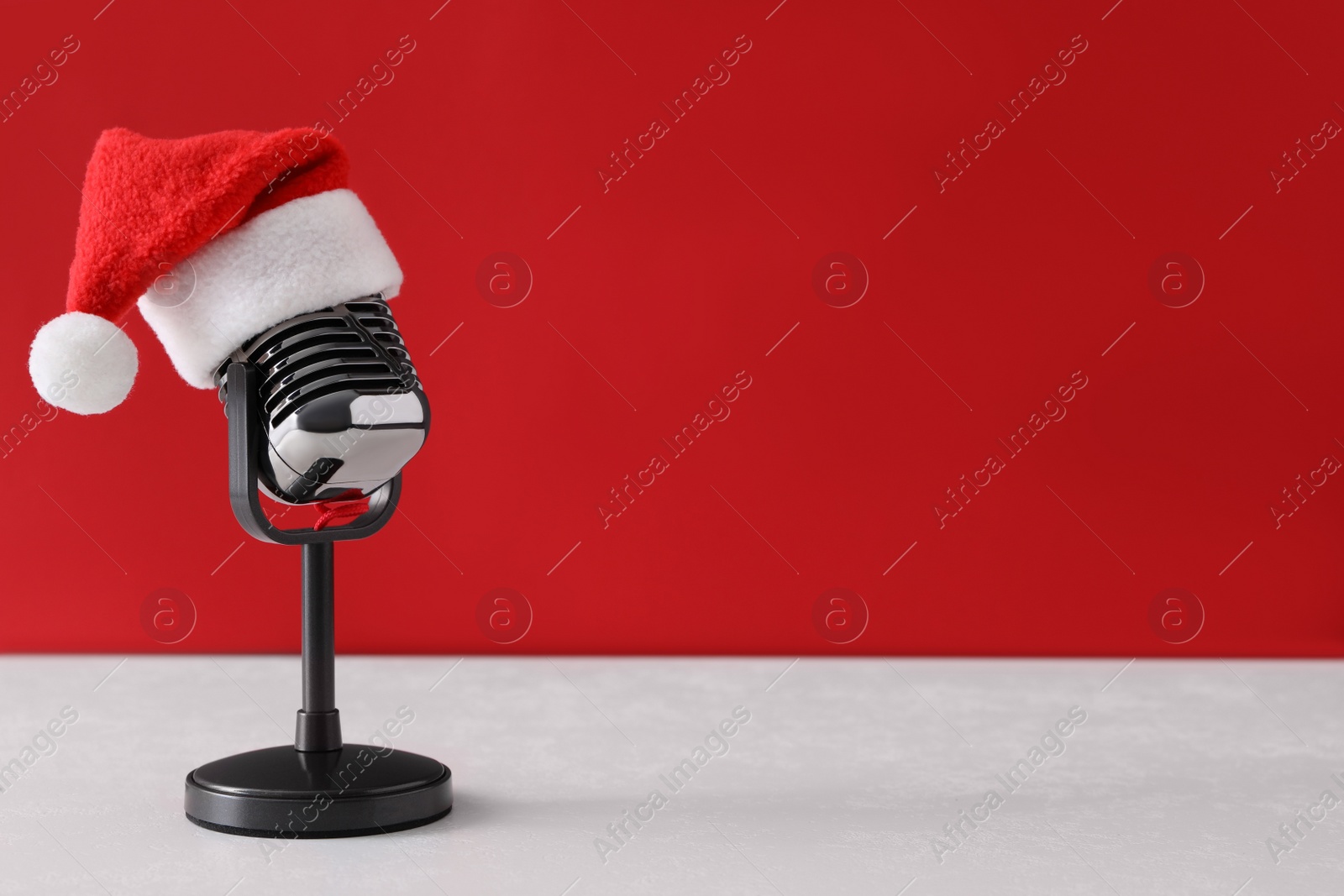 Photo of Retro microphone with Santa hat on table against red background, space for text. Christmas music