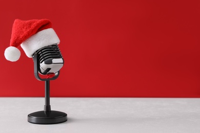 Photo of Retro microphone with Santa hat on table against red background, space for text. Christmas music