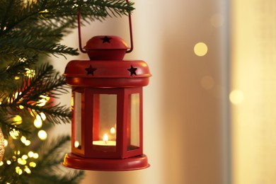 Photo of Christmas lantern with burning candle on fir tree indoors, closeup. Space for text