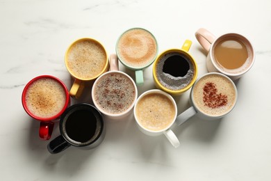 Photo of Many cups with different aromatic coffee on white marble table, flat lay