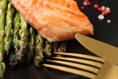 Tasty grilled salmon with asparagus and cutlery on table, closeup