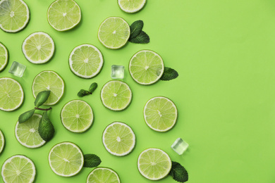 Photo of Flat lay composition with slices of fresh juicy limes on green background. Space for text