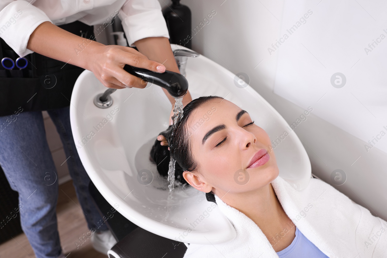 Photo of Professional hairdresser washing woman's hair in beauty salon, closeup