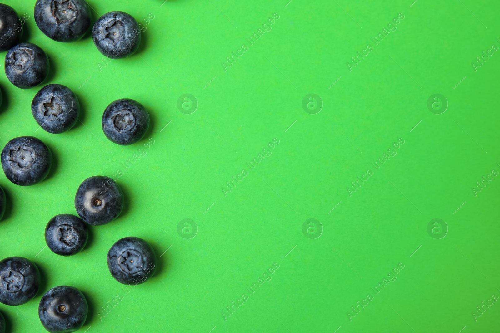 Photo of Tasty ripe blueberries on green background, flat lay with space for text