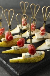 Tasty canapes with pears, blue cheese and prosciutto on grey table, closeup