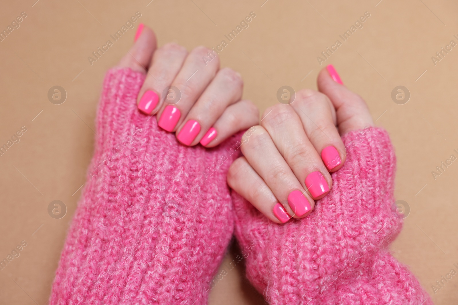 Photo of Woman showing her manicured hands with pink nail polish on dark beige background, closeup