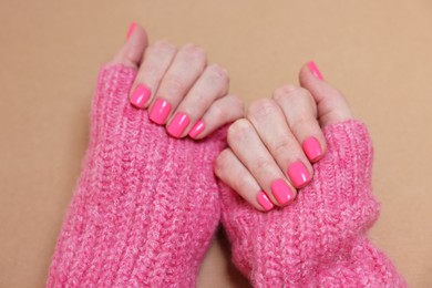 Woman showing her manicured hands with pink nail polish on dark beige background, closeup