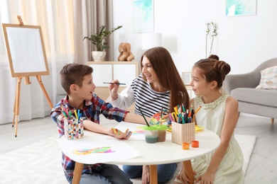 Young woman and children having fun with paints at table indoors