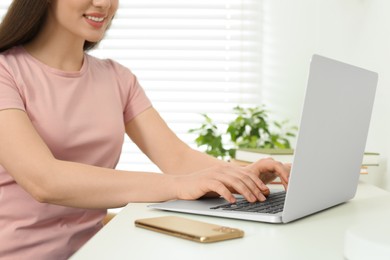 Home workplace. Woman typing on laptop at white desk indoors, closeup