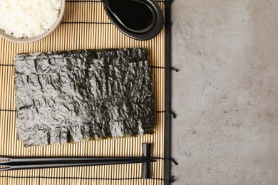 Photo of Dry nori sheets, rice, soy sauce and chopsticks on grey table, flat lay. Space for text
