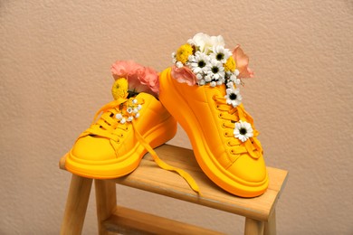 Image of Orange shoes with beautiful flowers on wooden stand against beige background