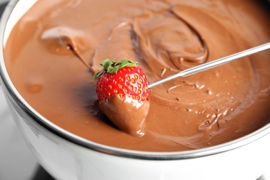 Dipping strawberry into pot with tasty chocolate fondue, closeup