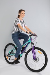 Happy young woman riding bicycle on grey background