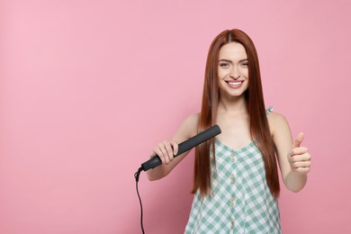 Photo of Beautiful woman using hair iron and showing thumbs up on pink background, space for text