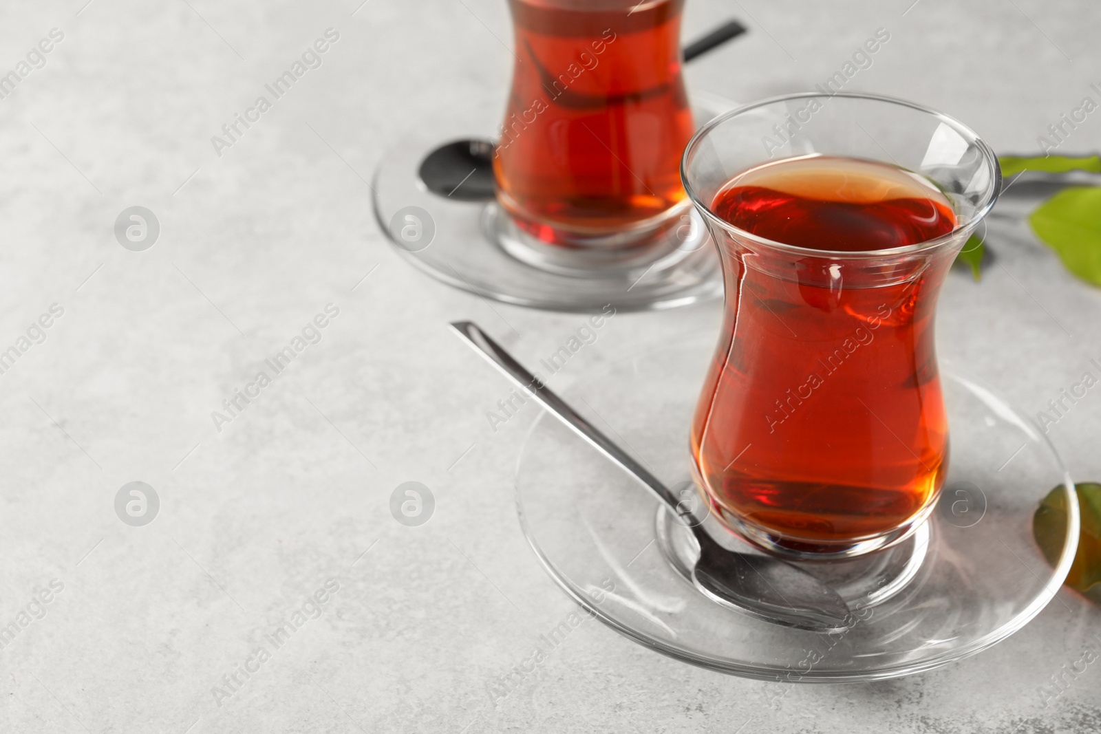 Photo of Glasses with traditional Turkish tea and green leaves on light grey table. Space for text