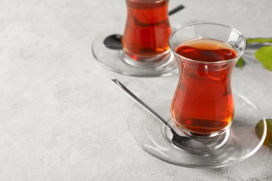 Photo of Glasses with traditional Turkish tea and green leaves on light grey table. Space for text