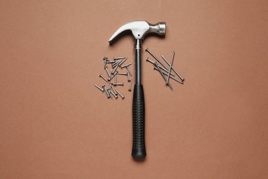 Hammer and metal nails on brown background, top view