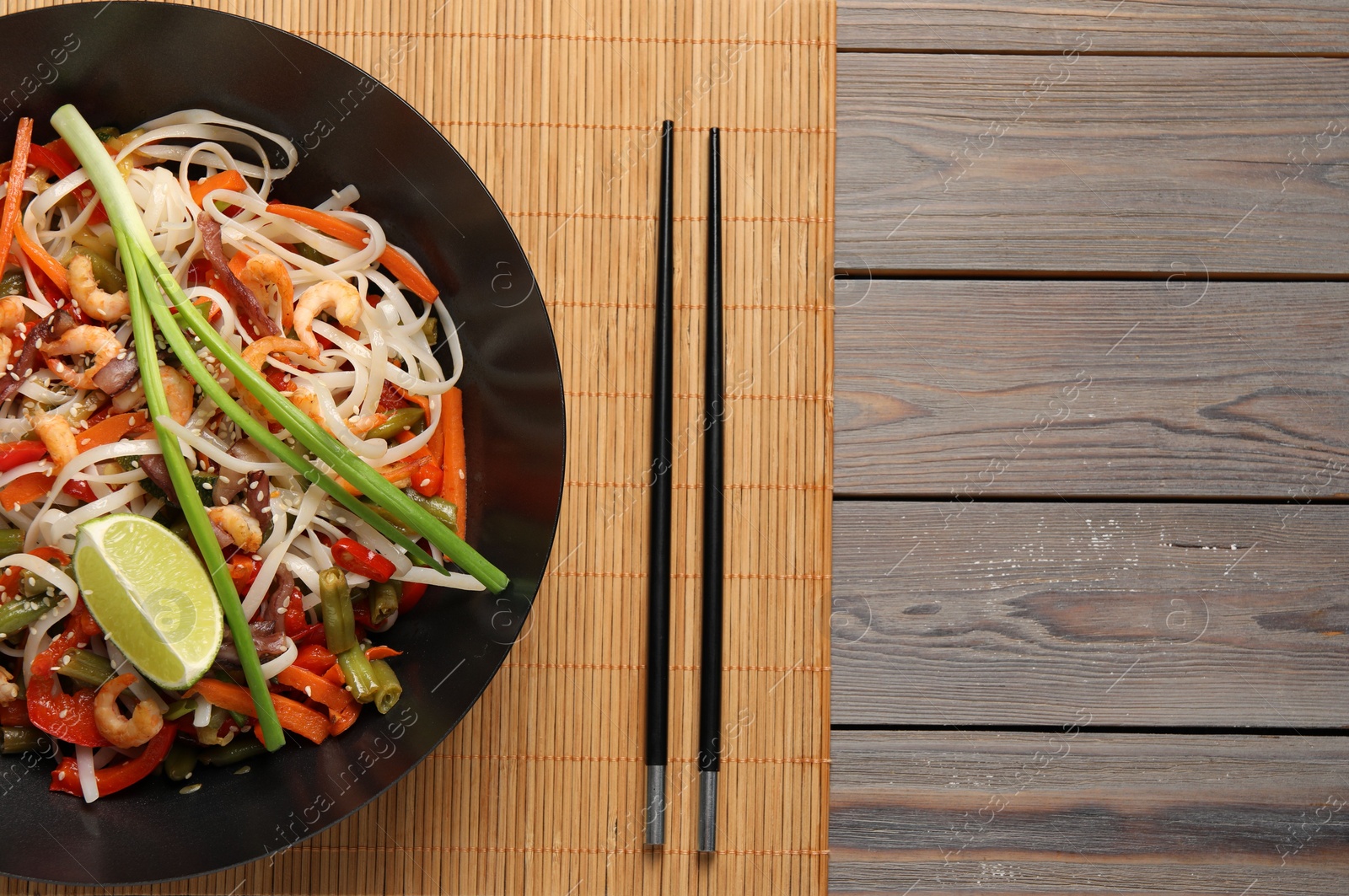Photo of Shrimp stir fry with noodles and vegetables in wok on wooden table, top view. Space for text