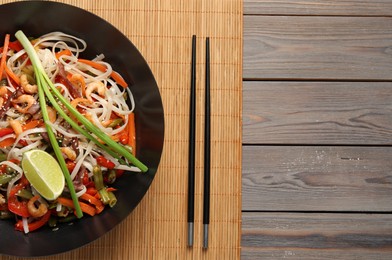 Shrimp stir fry with noodles and vegetables in wok on wooden table, top view. Space for text