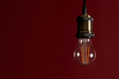 Photo of Pendant lamp with light bulb against dark red background, space for text