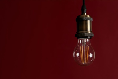 Pendant lamp with light bulb against dark red background, space for text