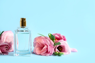 Photo of Bottleperfume and beautiful flowers on light blue background. Space for text