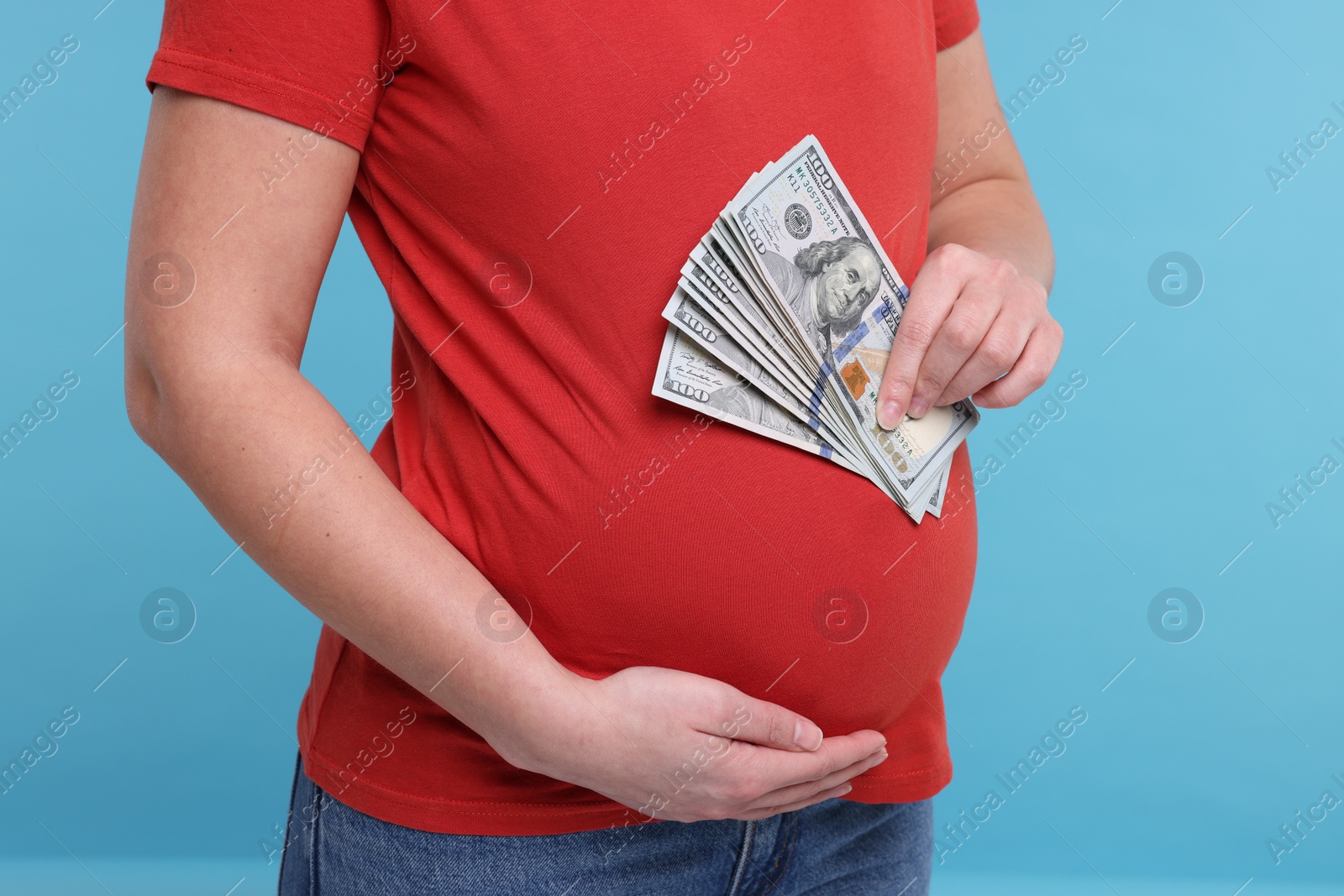 Photo of Surrogate mother. Pregnant woman with dollar banknotes on light blue background, closeup