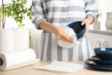 Photo of Woman wiping ceramic bowl with paper towel indoors, closeup