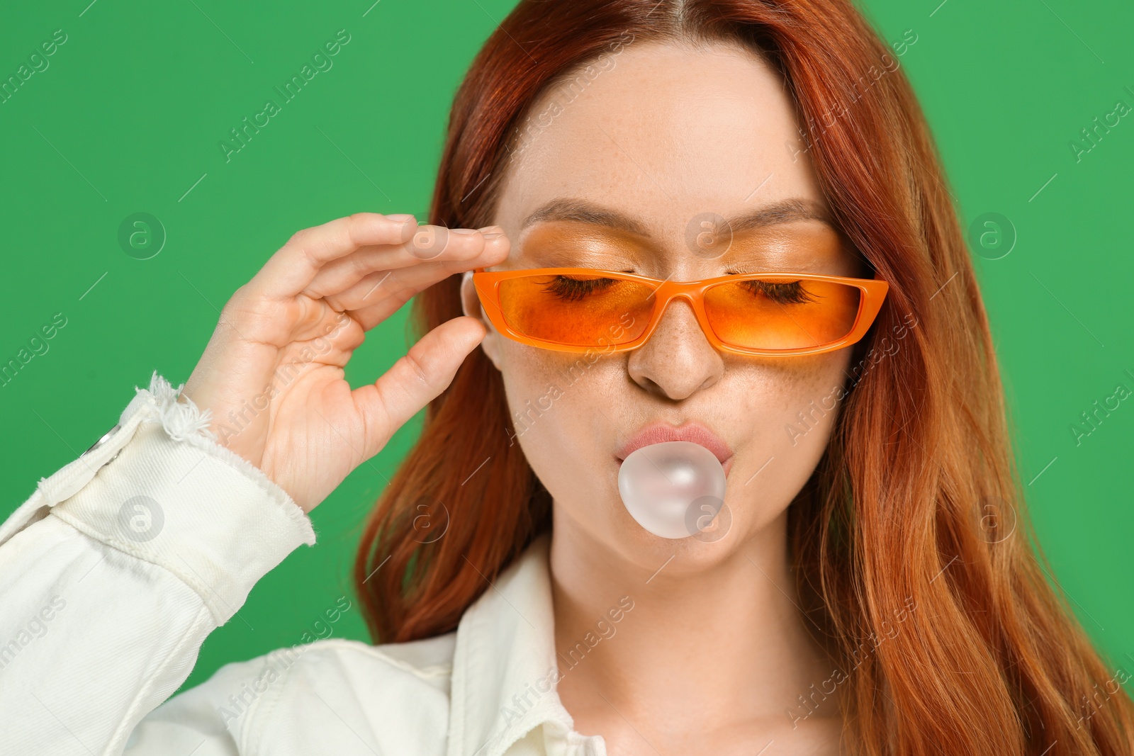 Photo of Beautiful woman in sunglasses blowing bubble gum on green background