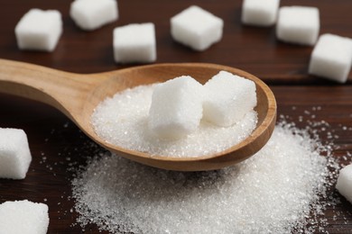 Photo of Spoon with sugar in granules and cubes on wooden table, closeup