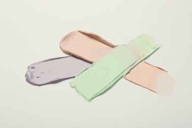 Photo of Strokes of pink, green and purple color correcting concealers on white background