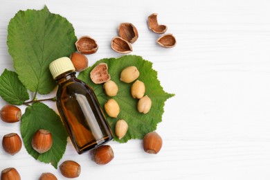 Photo of Bottle of hazelnut essential oil and nuts on white wooden table, flat lay. Space for text