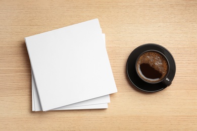 Photo of Blank paper sheets for brochure and cup of coffee on wooden background, flat lay. Mock up