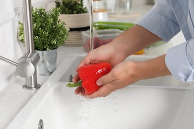 Man washing fresh bell pepper in kitchen, closeup