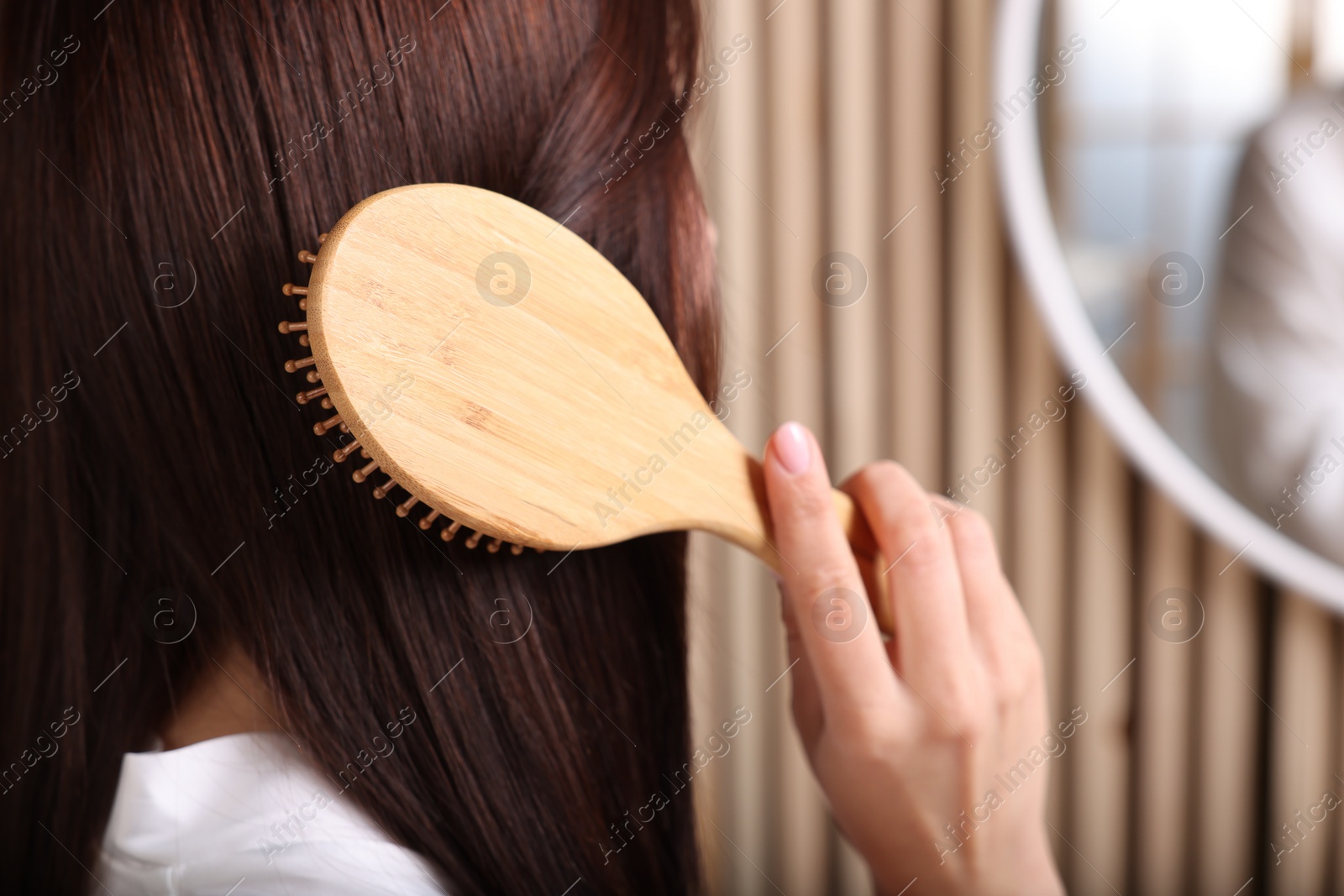 Photo of Beautiful woman brushing her hair near mirror in room, closeup. Space for text