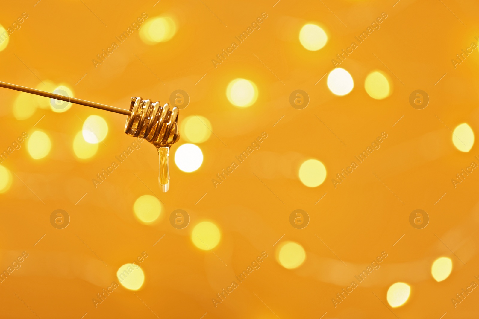 Photo of Honey dripping from dipper against blurred lights. Space for text