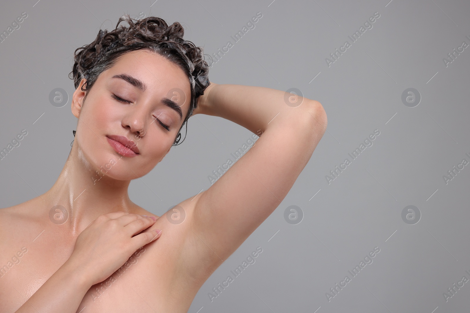 Photo of Beautiful woman washing hair on grey background. Space for text