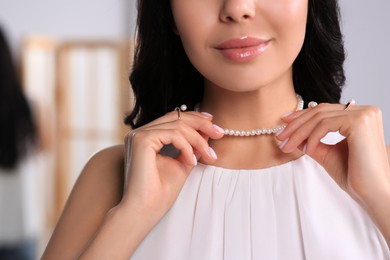 Photo of Young woman trying on elegant pearl necklace indoors, closeup