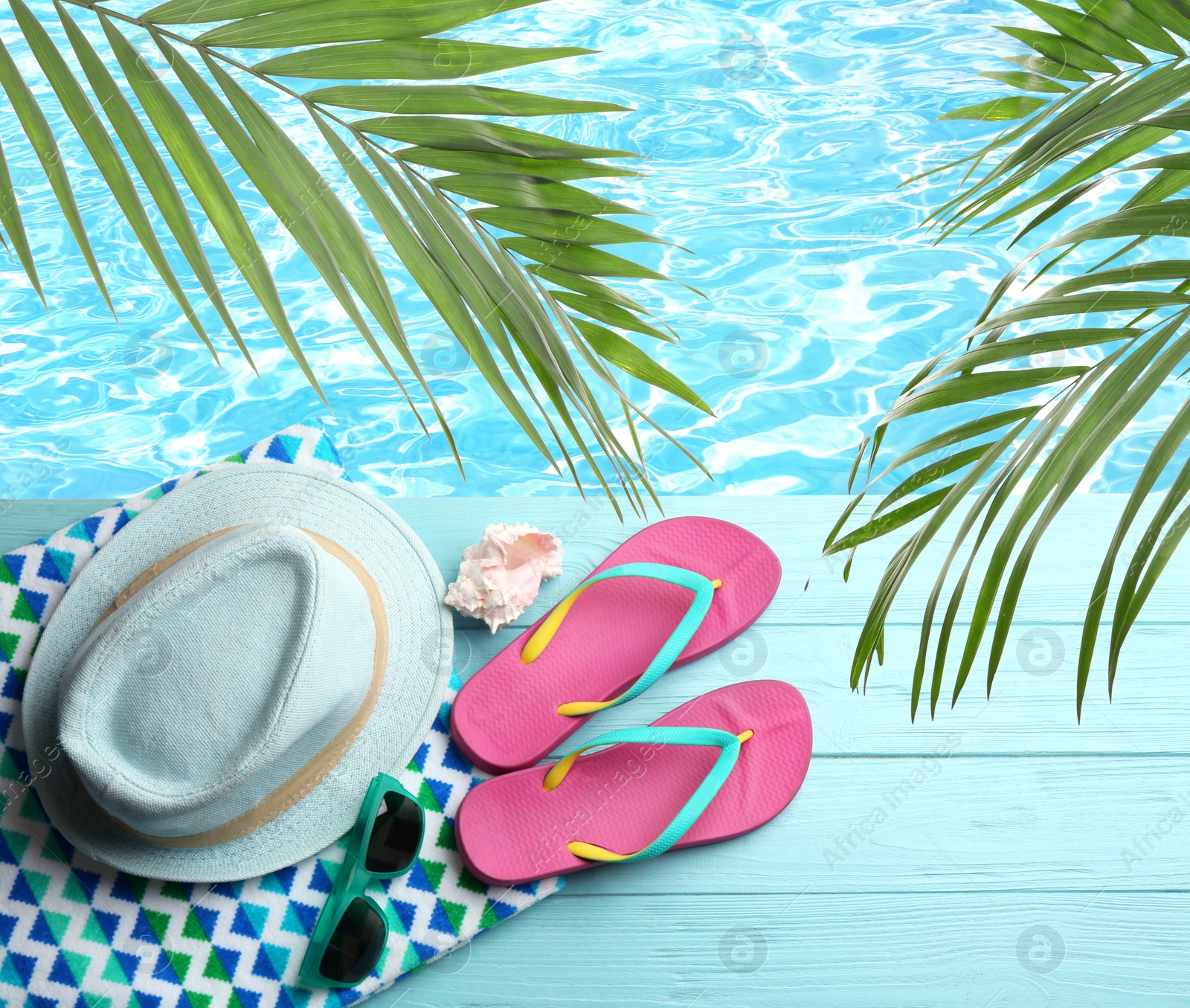 Image of Beach accessories on light blue wooden surface near swimming pool, above view