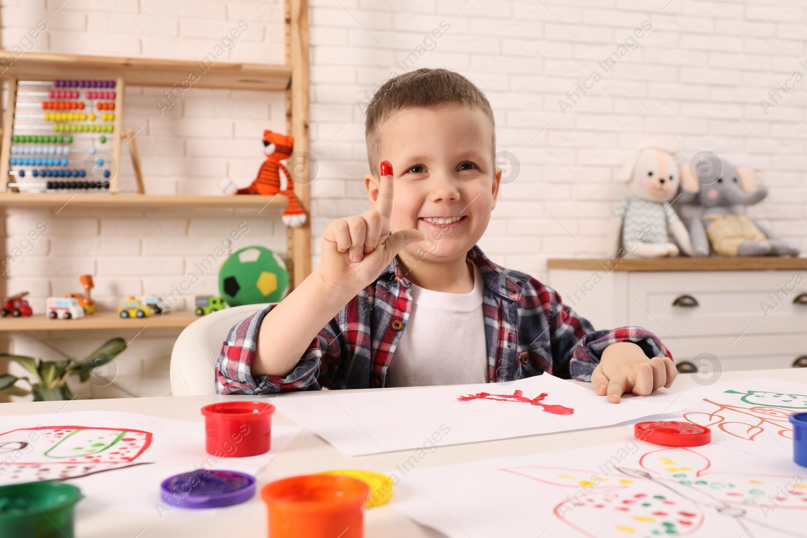 Photo of Little boy painting with finger at white table indoors